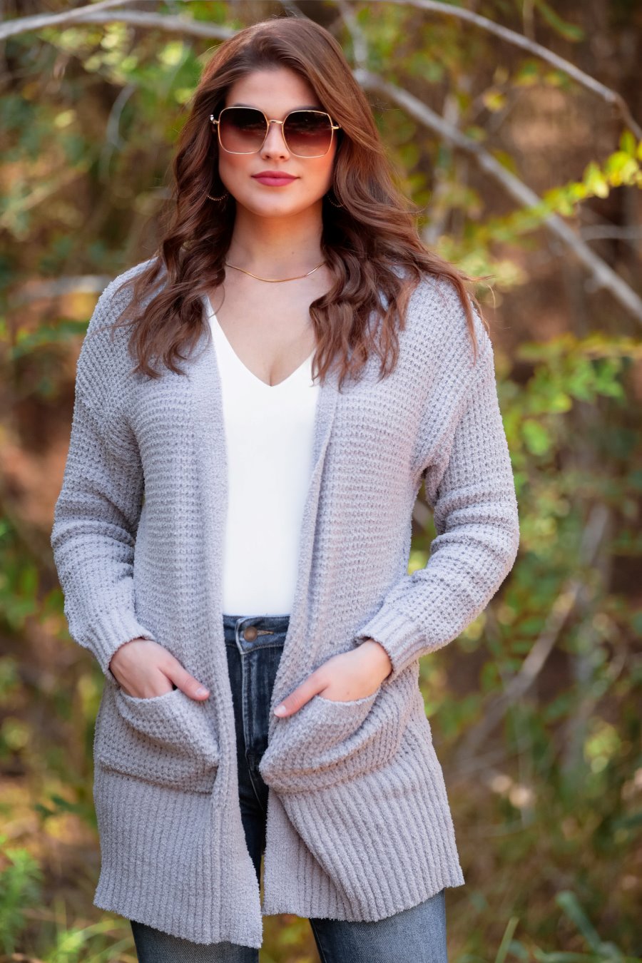 long-sleeve cardigan made of a soft knit material with front pockets and a draped open front silhouette that ends in a straight hemline on a grey fabric