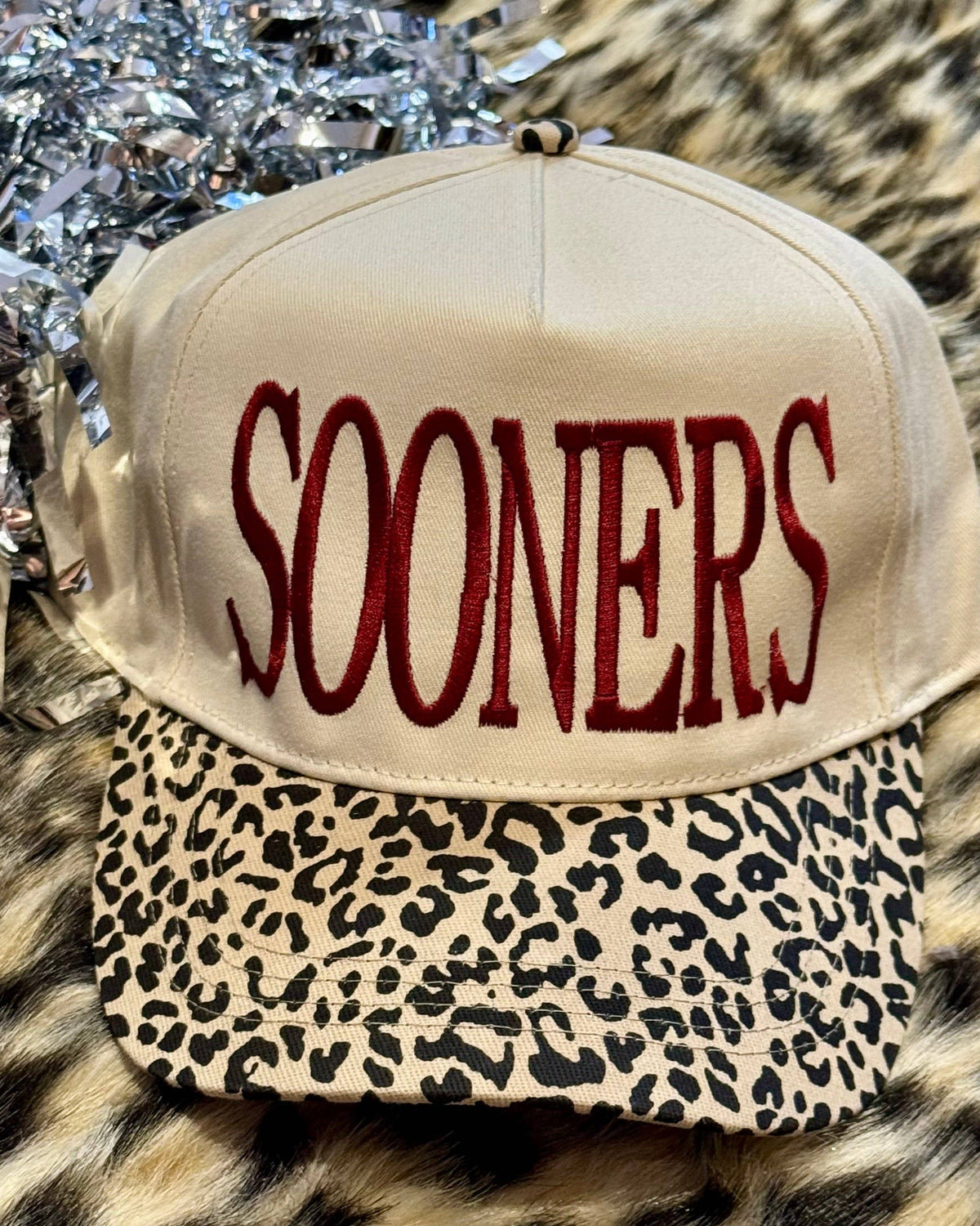 a lightweight unisex two-tone hat with embroidered crimson 'SOONERS' lettering, cream structured front, curved contrasting black leopard bill, coordinating leopard top button, and adjustable snap-back closure