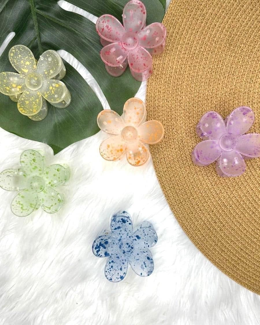 Colorful flower-shaped hair clips on a straw hat with green leaves and white fabric background