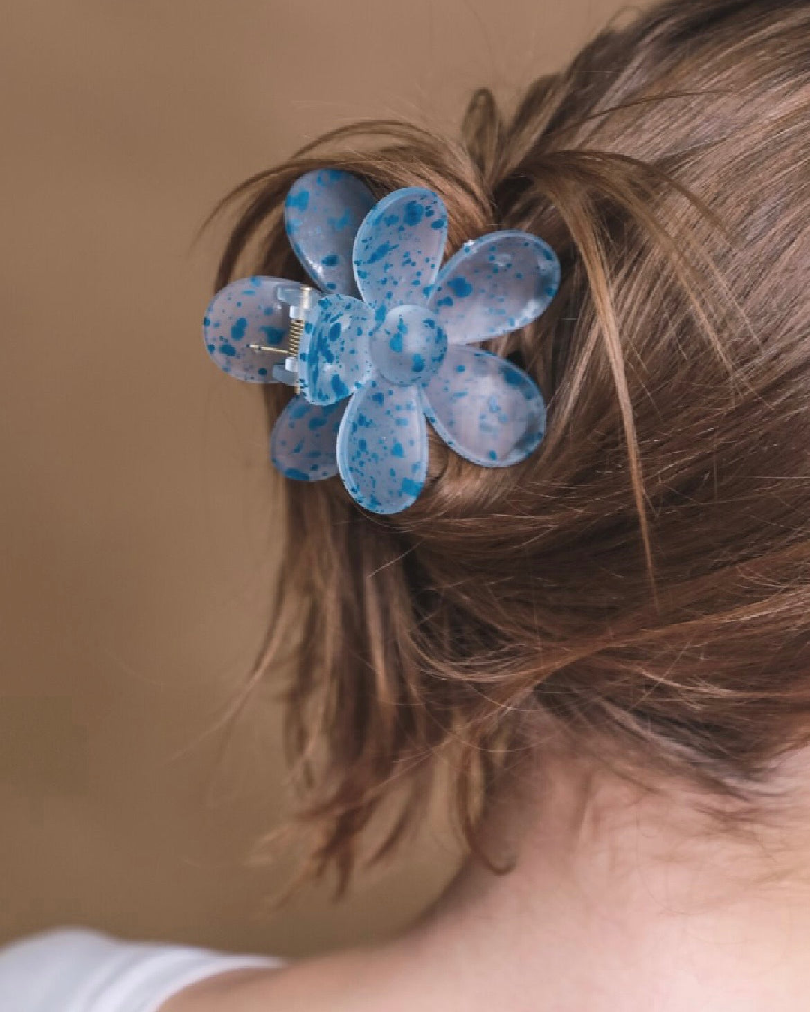 Blue flower-shaped hair clip in a person's hair against a brown background