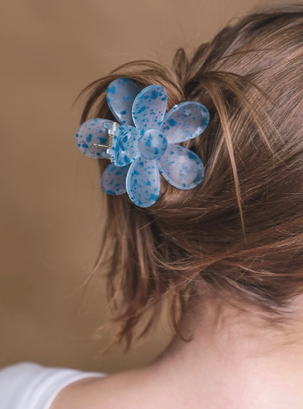 Blue flower-shaped hair clip in a person's hair against a brown background