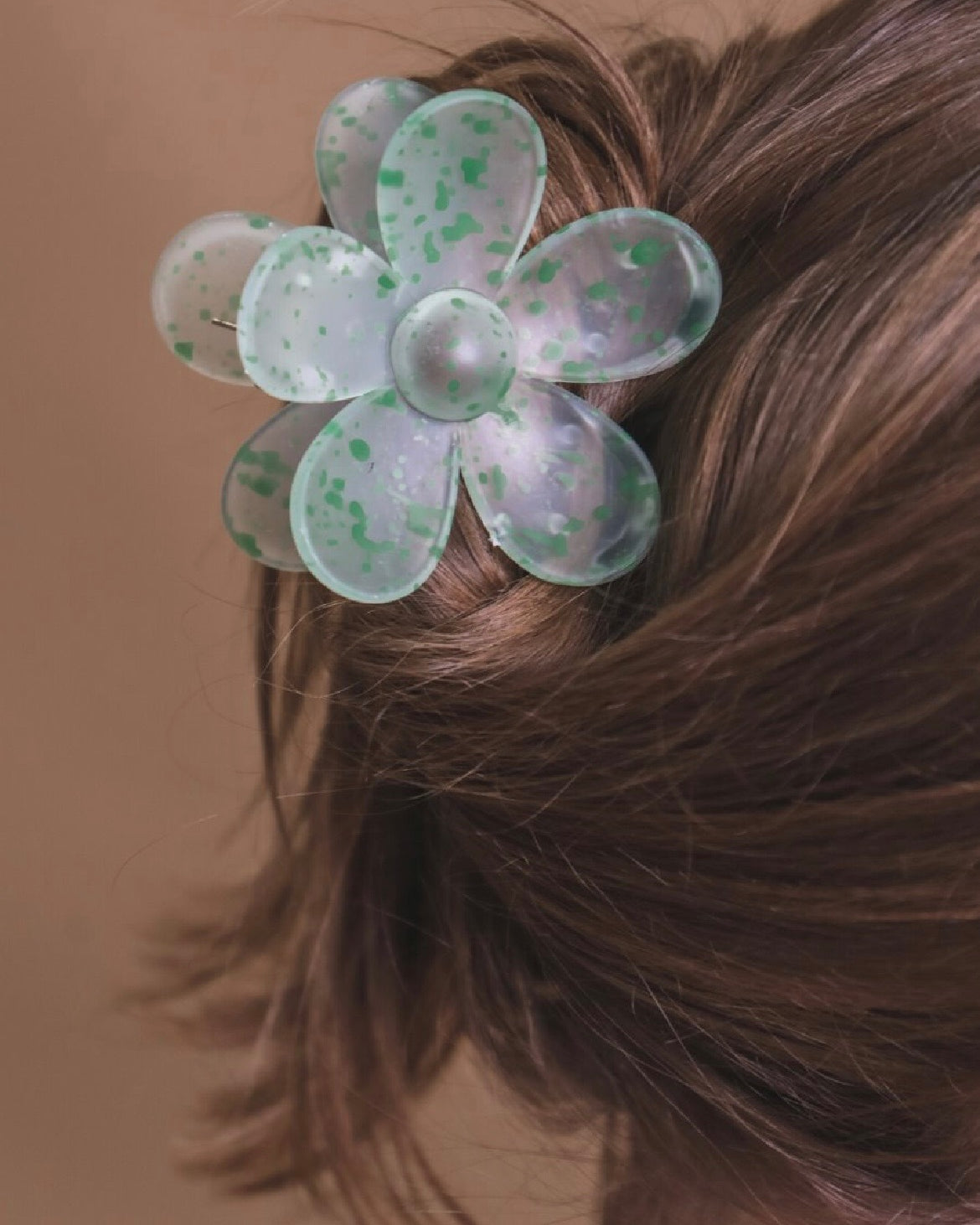 Green flower-shaped hair clip in a person's hair against a brown background
