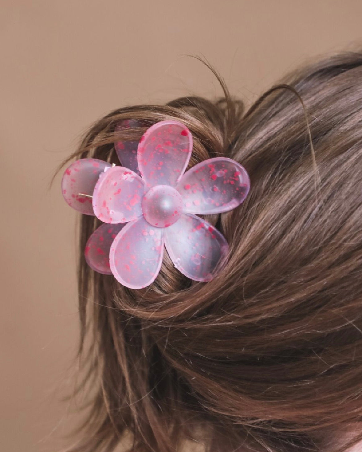 Pink flower-shaped hair clip in a person's hair against a brown background