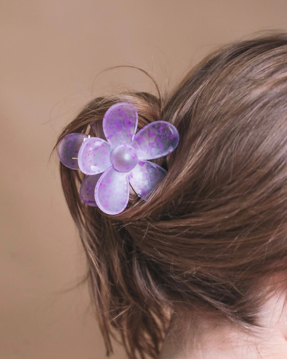 Purple flower-shaped hair clip in a person's hair against a brown background