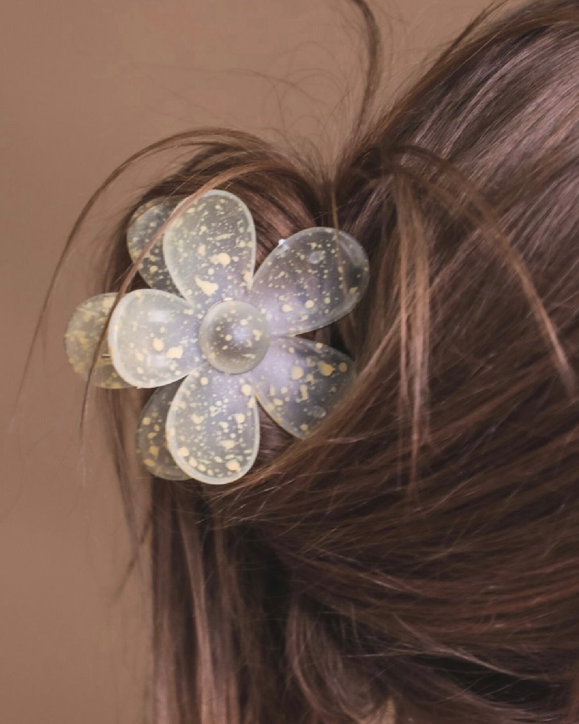 Yellow flower-shaped hair clip in a person's hair against a brown background