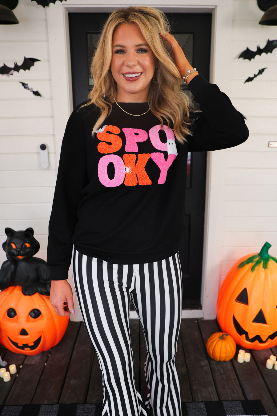 a black long-sleeve pullover made of ultra soft luxe material with bold plush chenille 'SPOOKY' patch lettering (orange and pink), white embroidered character accents (tiny bat, ghost and spider), ribbed cuffs, a banded hem, and a relaxed fit for a classic silhouette