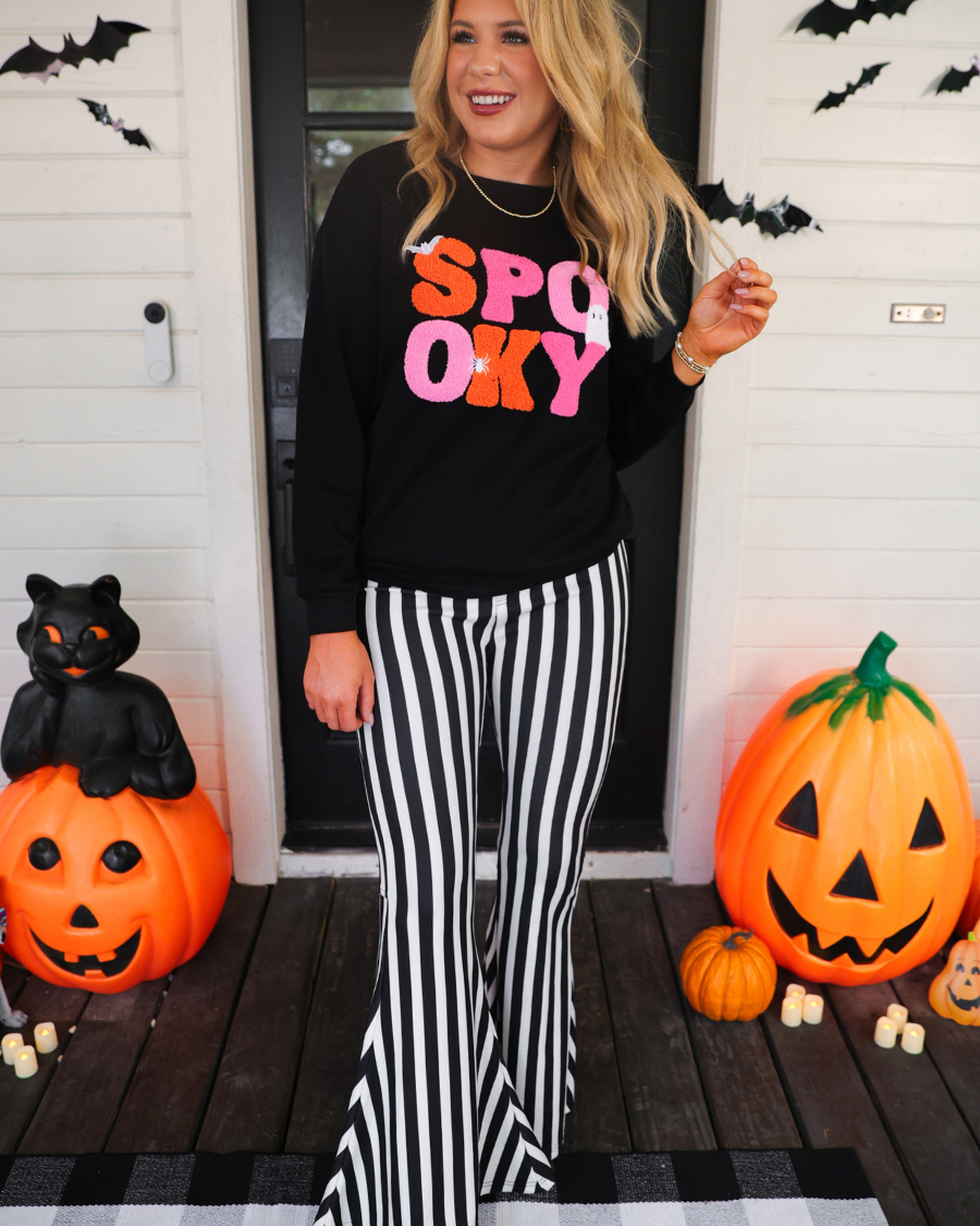 a black long-sleeve pullover made of ultra soft luxe material with bold plush chenille 'SPOOKY' patch lettering (orange and pink), white embroidered character accents (tiny bat, ghost and spider), ribbed cuffs, a banded hem, and a relaxed fit for a classic silhouette