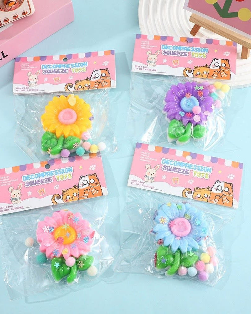 a flower-shaped decompression squishy toy with glossy petals, green leaves, mini decorative accents, and pastel pom poms in blue, pink, purple, and yellow