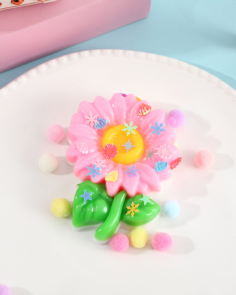 a pink flower-shaped decompression squishy toy with glossy petals, green leaves, mini decorative accents, and pastel pom poms
