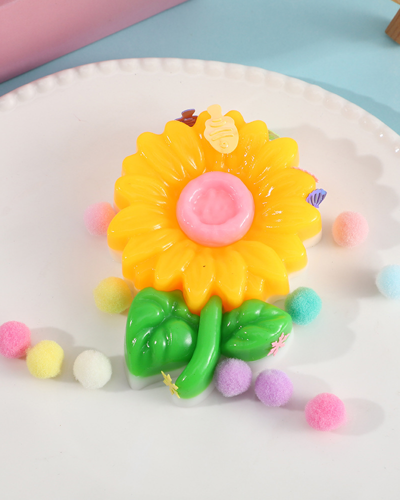 a yellow flower-shaped decompression squishy toy with glossy petals, green leaves, mini decorative accents, and pastel pom poms