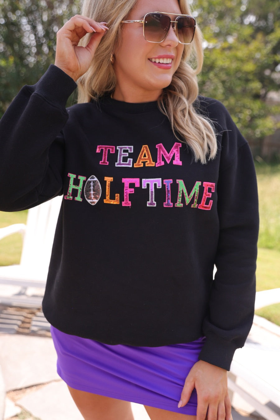 black long-sleeve sweatshirt made from soft mid-weight fabric with a crew neckline, straight hem, and bold multicolored varsity-style chenille patches that spell out 'TEAM HALFTIME' across the front chest