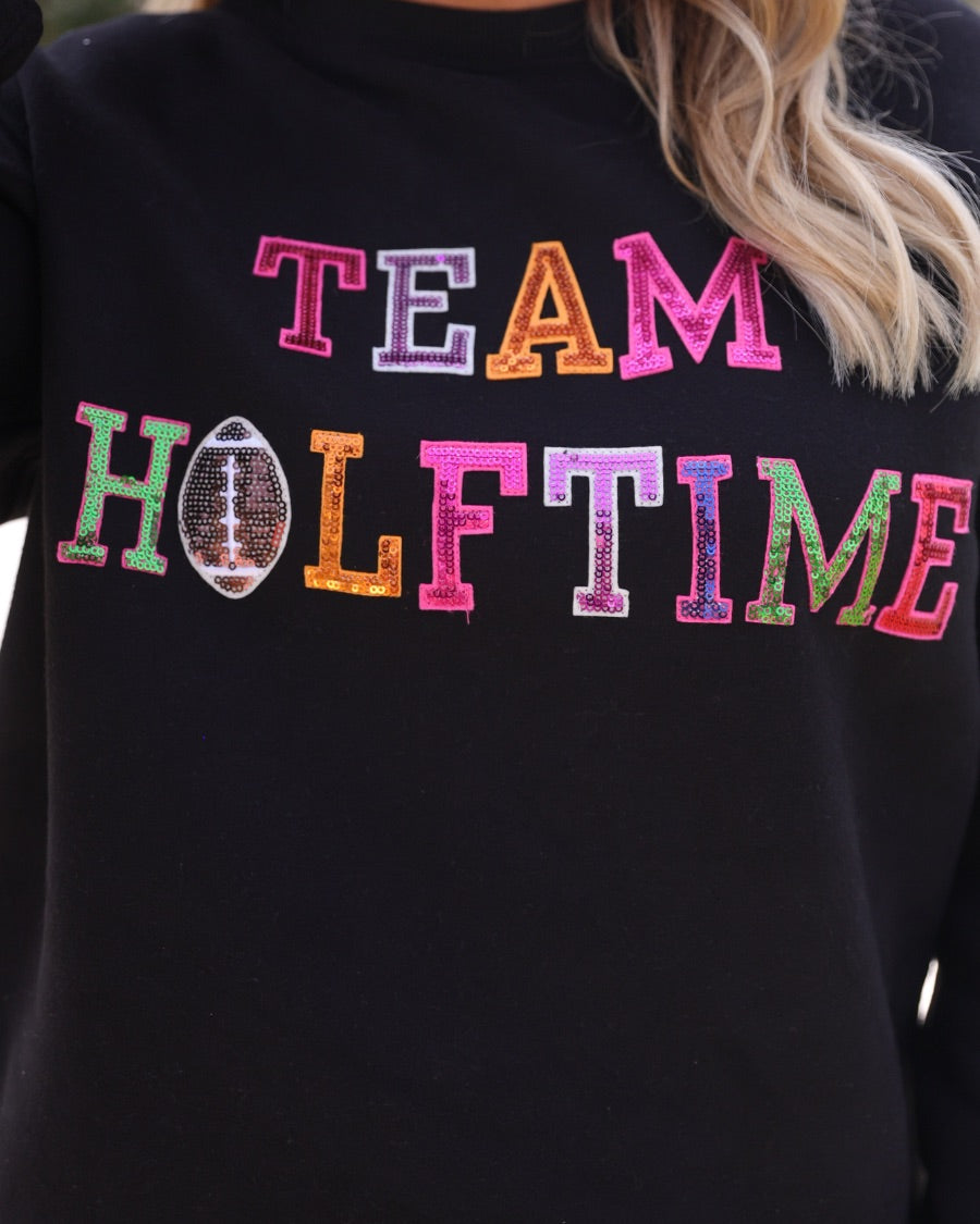 black long-sleeve sweatshirt made from soft mid-weight fabric with a crew neckline, straight hem, and bold multicolored varsity-style chenille patches that spell out 'TEAM HALFTIME' across the front chest