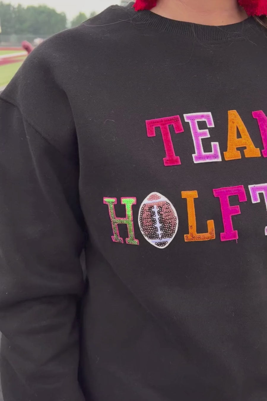 black long-sleeve sweatshirt made from soft mid-weight fabric with a crew neckline, straight hem, and bold multicolored varsity-style chenille patches that spell out 'TEAM HALFTIME' across the front chest