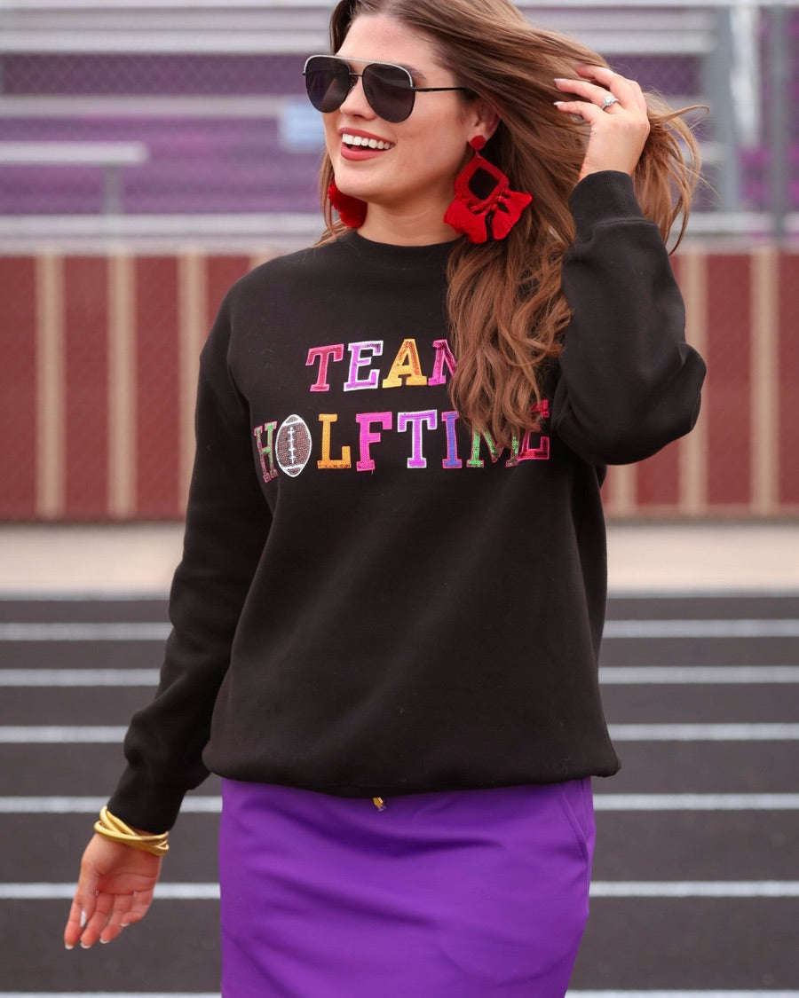 black long-sleeve sweatshirt made from soft mid-weight fabric with a crew neckline, straight hem, and bold multicolored varsity-style chenille patches that spell out 'TEAM HALFTIME' across the front chest