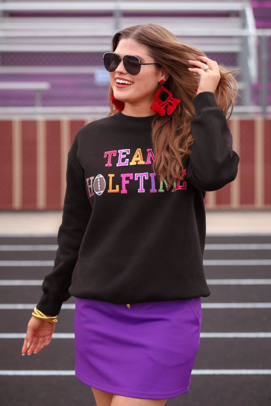 black long-sleeve sweatshirt made from soft mid-weight fabric with a crew neckline, straight hem, and bold multicolored varsity-style chenille patches that spell out 'TEAM HALFTIME' across the front chest