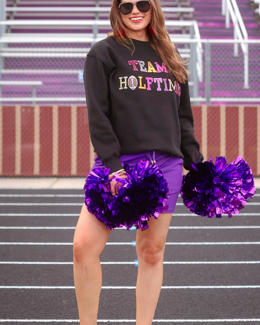 black long-sleeve sweatshirt made from soft mid-weight fabric with a crew neckline, straight hem, and bold multicolored varsity-style chenille patches that spell out 'TEAM HALFTIME' across the front chest