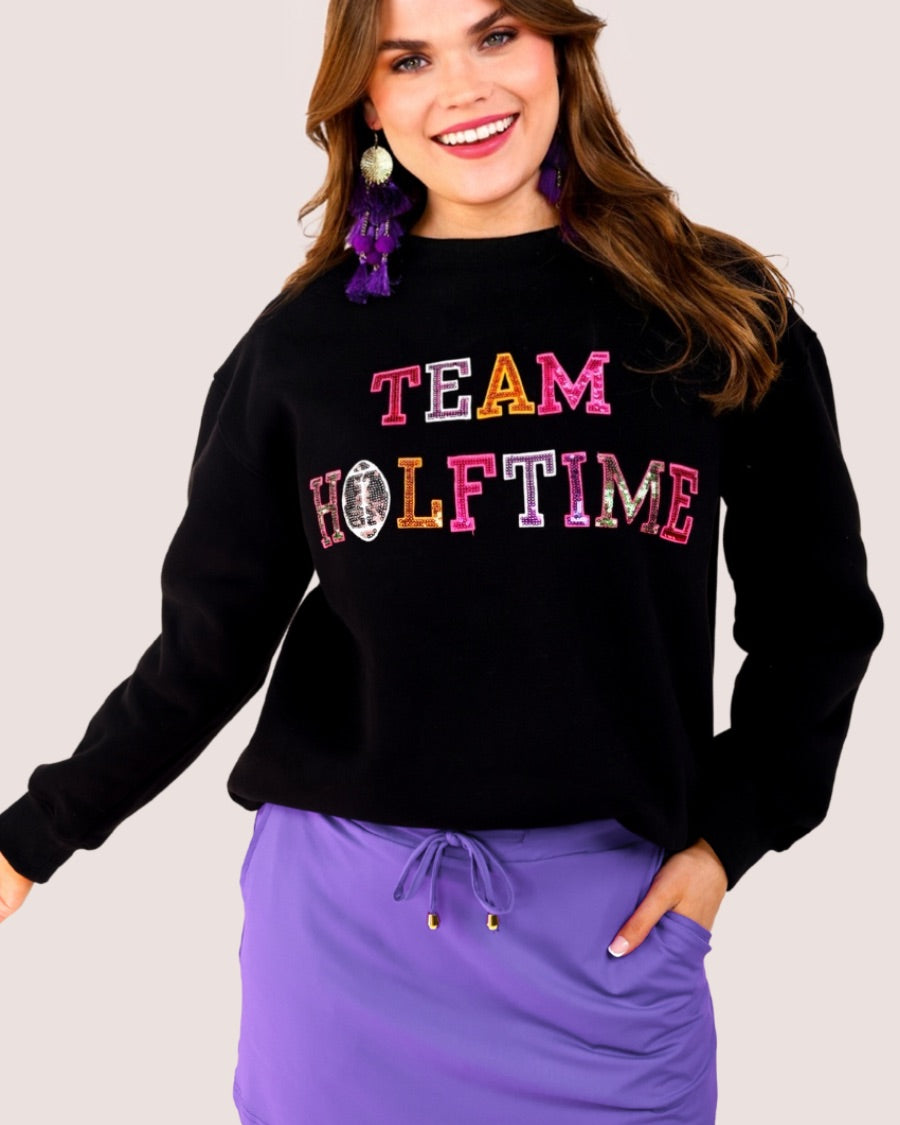 black long-sleeve sweatshirt made from soft mid-weight fabric with a crew neckline, straight hem, and bold multicolored varsity-style chenille patches that spell out 'TEAM HALFTIME' across the front chest
