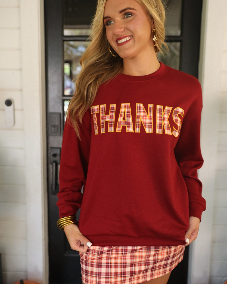 long-sleeve burgundy pullover with plaid 'THANKS' letters outlined in embroidery on a soft fabric