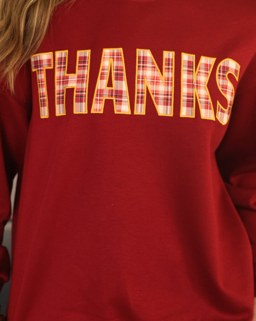 long-sleeve burgundy pullover with plaid 'THANKS' letters outlined in embroidery on a soft fabric