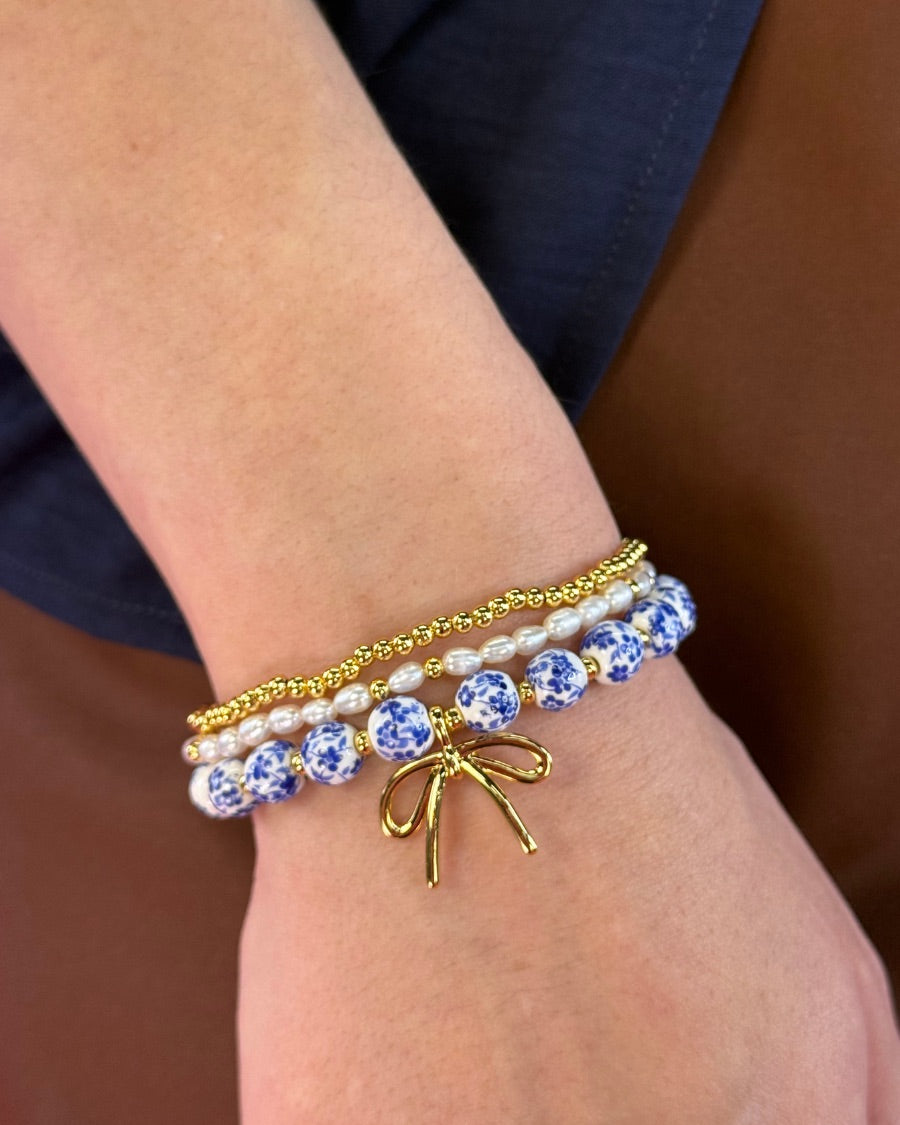 three-piece bracelet set with a charming mix of brass, sheer pearls, floral-patterned beads, and a dainty bow accent