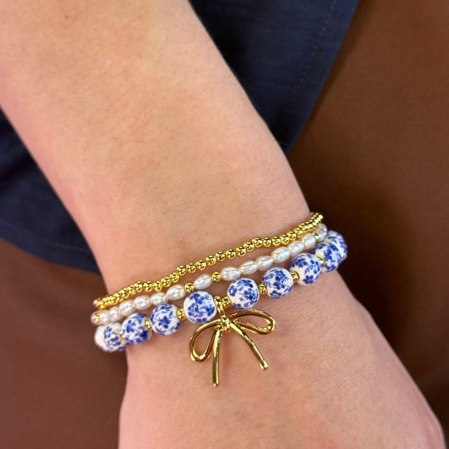 three-piece bracelet set with a charming mix of brass, sheer pearls, floral-patterned beads, and a dainty bow accent