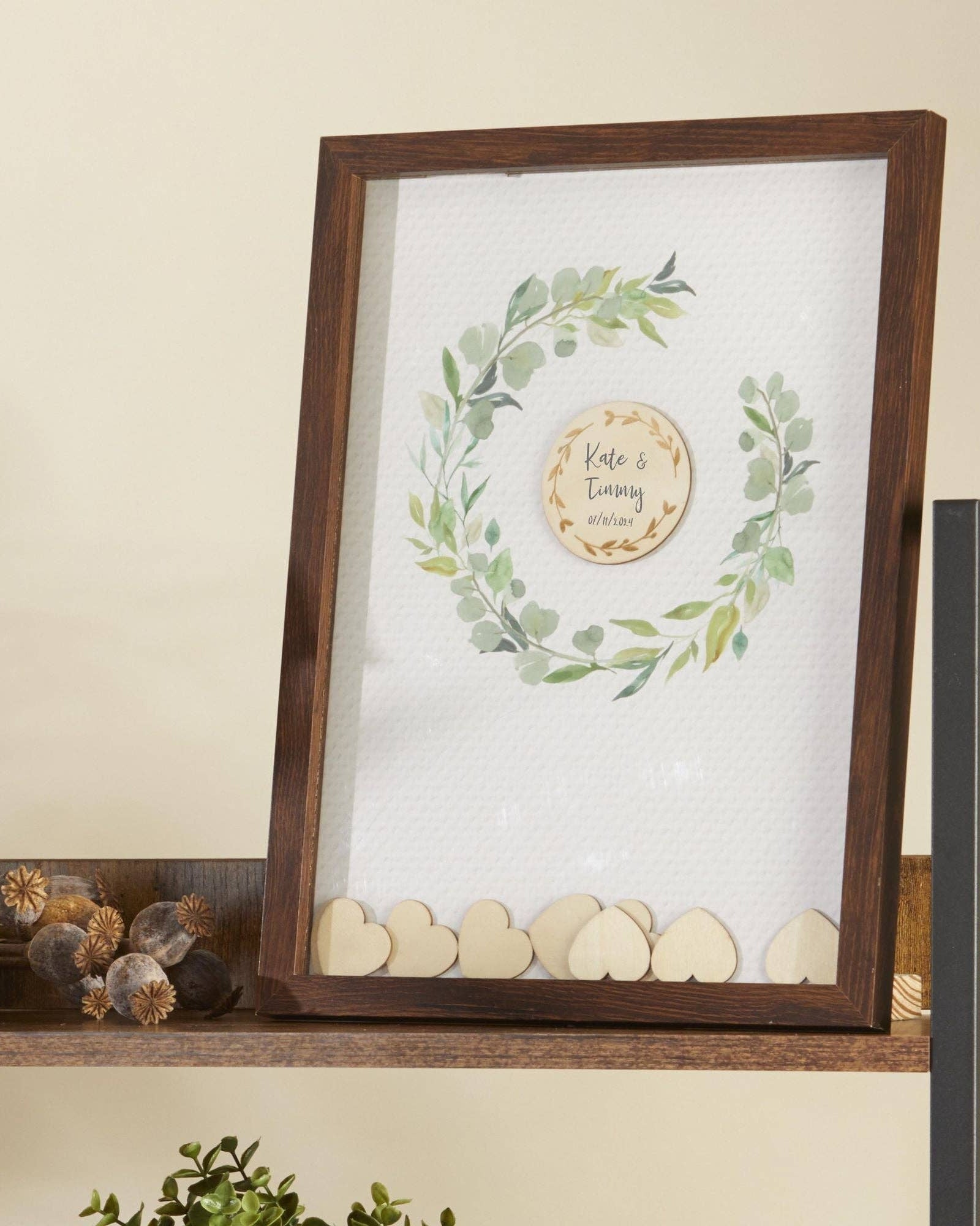 Framed artwork with greenery and wooden hearts on a shelf.