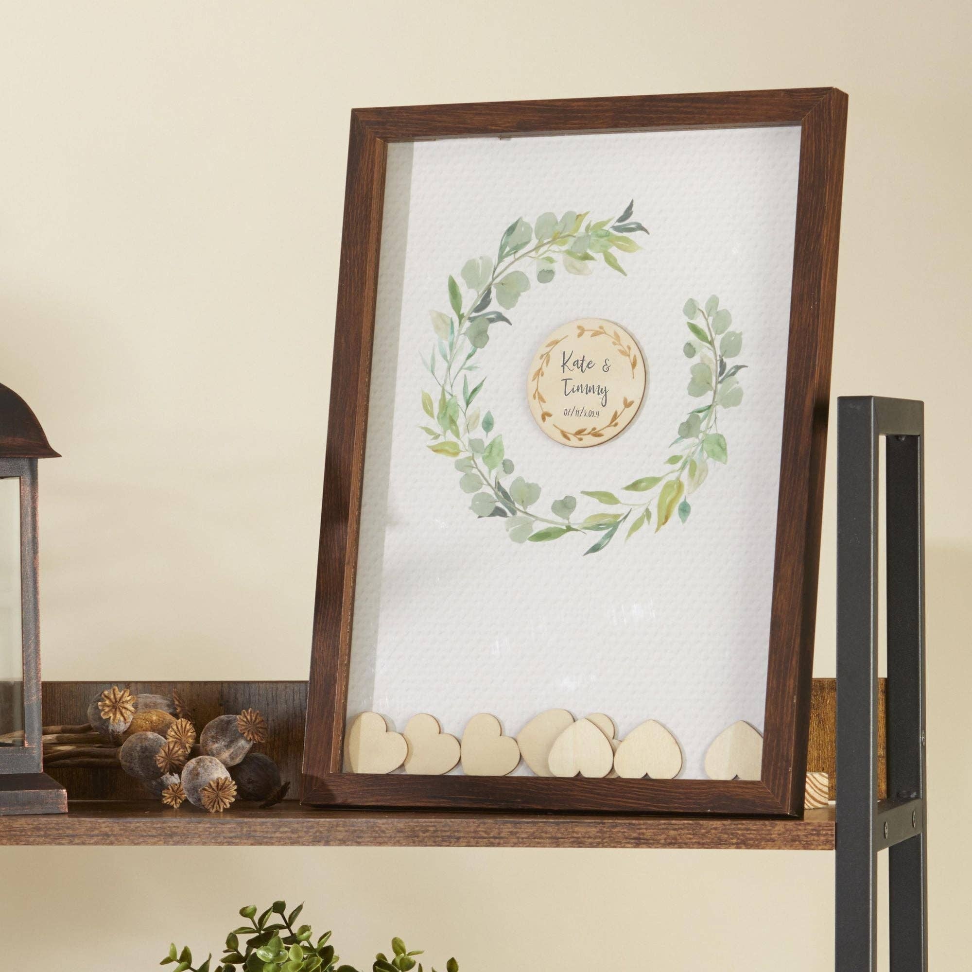 Framed artwork with greenery and wooden hearts on a shelf.