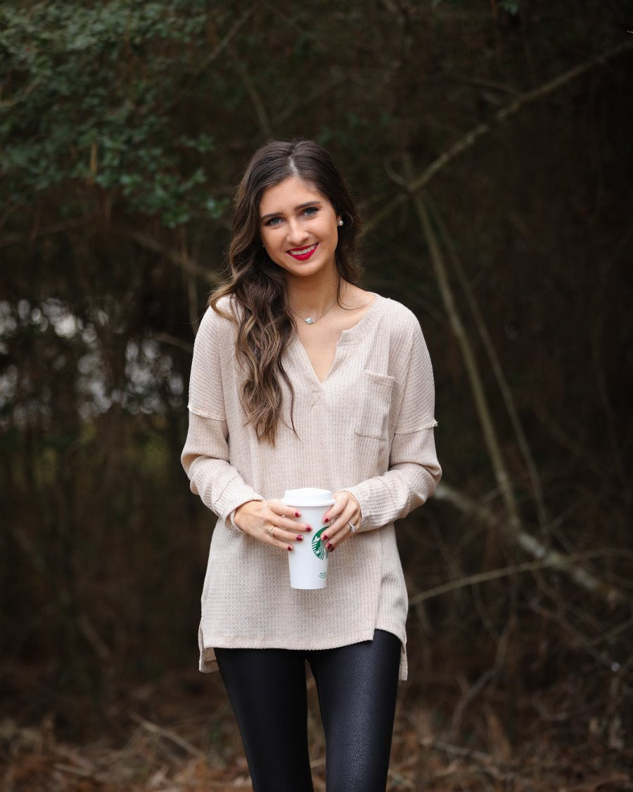 made in the USA long-sleeve top crafted from soft material with waffle knit texturing, a drop shoulder, a v-neck neckline, a front chest pocket, a hi-low side split hem, and a relaxed fit that falls into a straight hemline in oatmeal