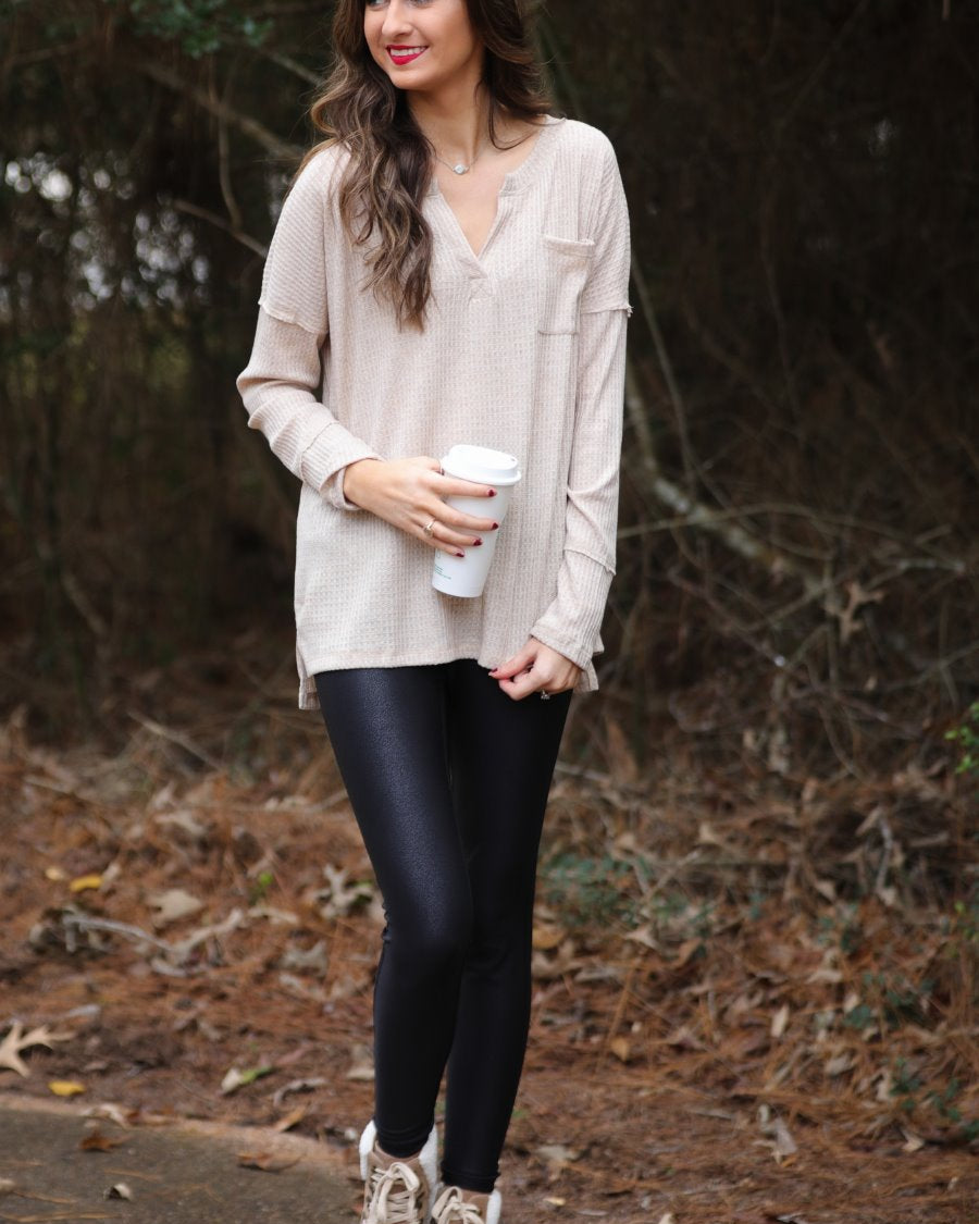 made in the USA long-sleeve top crafted from soft material with waffle knit texturing, a drop shoulder, a v-neck neckline, a front chest pocket, a hi-low side split hem, and a relaxed fit that falls into a straight hemline in oatmeal