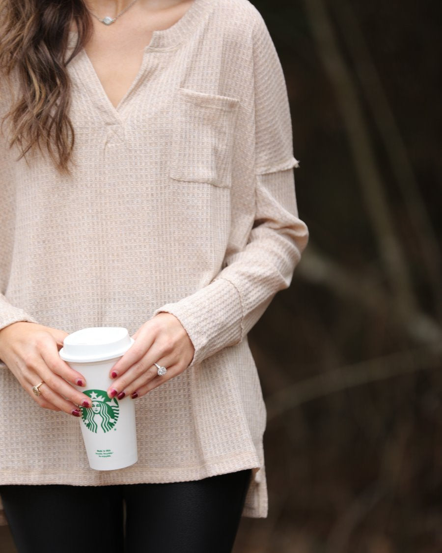 made in the USA long-sleeve top crafted from soft material with waffle knit texturing, a drop shoulder, a v-neck neckline, a front chest pocket, a hi-low side split hem, and a relaxed fit that falls into a straight hemline in oatmeal