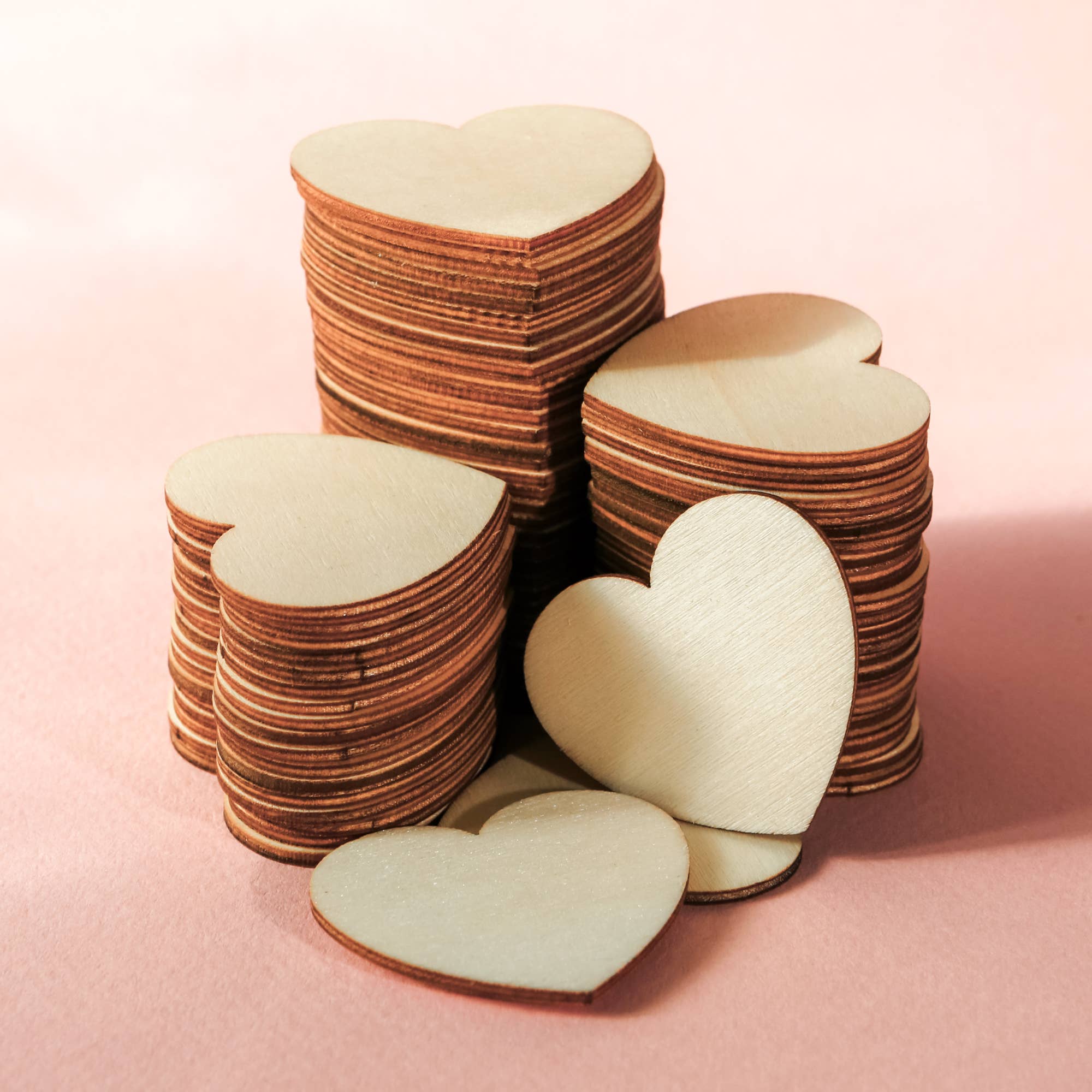 Stack of heart-shaped wooden cutouts on a pink background