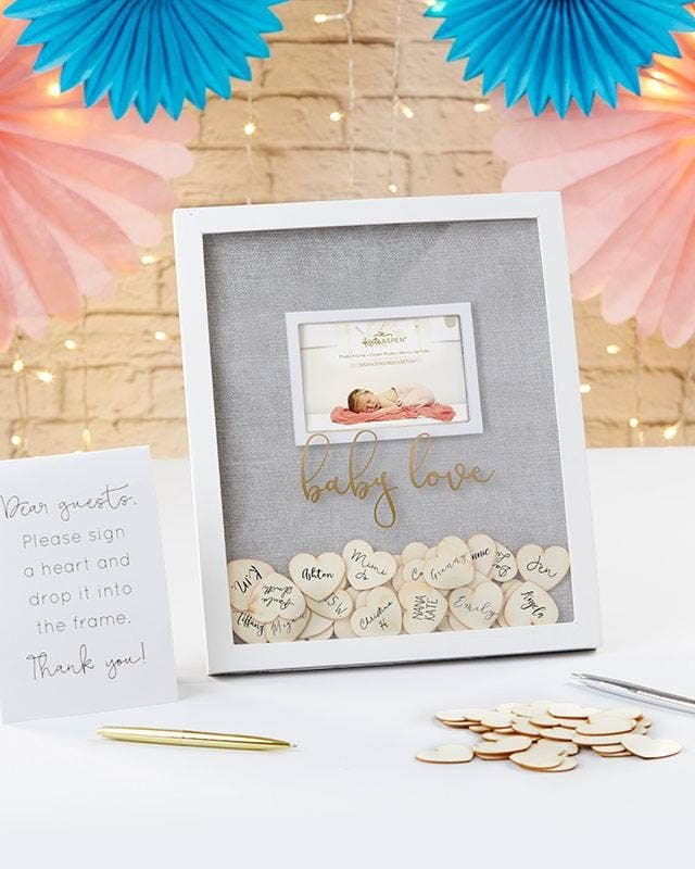 Decorative baby shower frame with heart-shaped confetti and a card on a table with festive decorations.