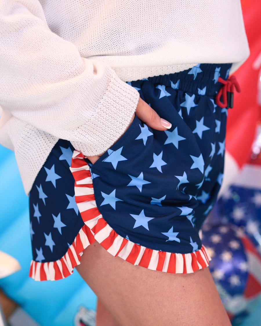 mid-rise relaxed fit activewear shorts with side pockets and a red tie waist drawstring finished with black aglets, designed on a two-tone blue star pattern print and red-and-white ruffle trim