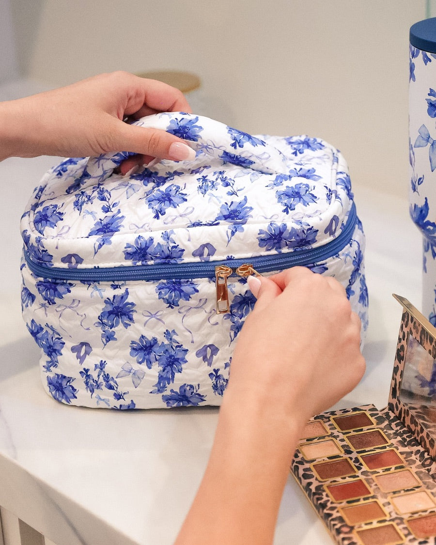 a structured bag with a spacious interior, a secure double zip around closure, a top handle, and gold accents on a quilted body in blue blossom (white/blue)