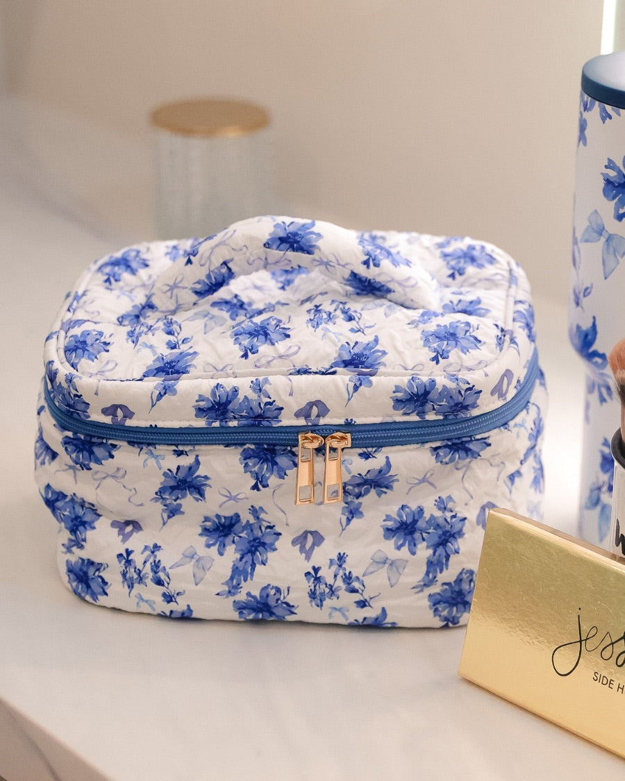 a structured bag with a spacious interior, a secure double zip around closure, a top handle, and gold accents on a quilted body in blue blossom (white/blue)