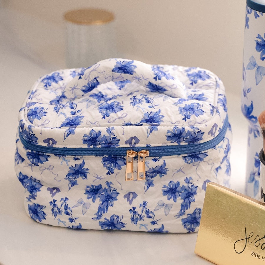 a structured bag with a spacious interior, a secure double zip around closure, a top handle, and gold accents on a quilted body in blue blossom (white/blue)