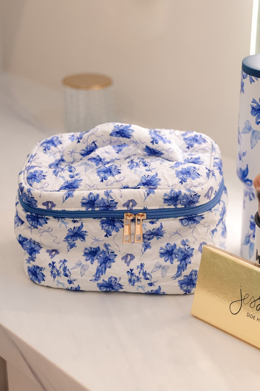 a structured bag with a spacious interior, a secure double zip around closure, a top handle, and gold accents on a quilted body in blue blossom (white/blue)