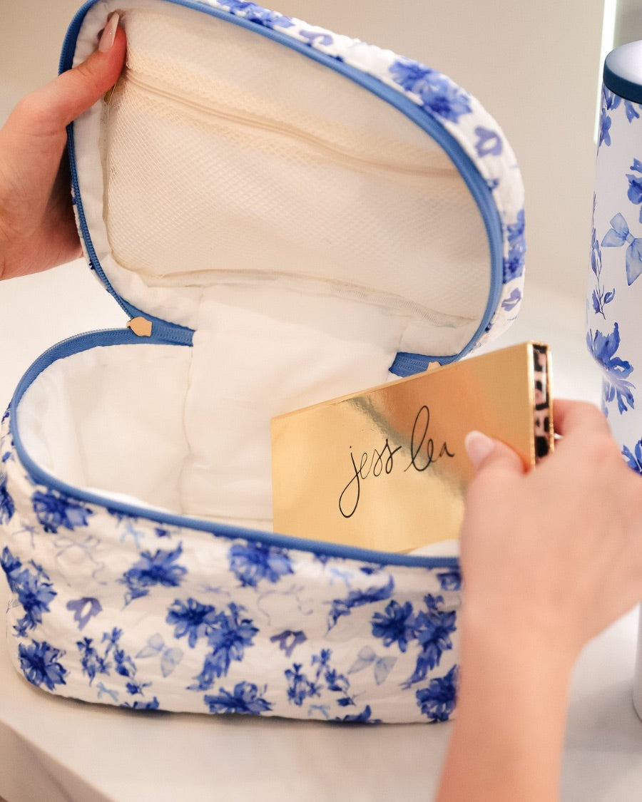 a structured bag with a spacious interior, a secure double zip around closure, a top handle, and gold accents on a quilted body in blue blossom (white/blue)