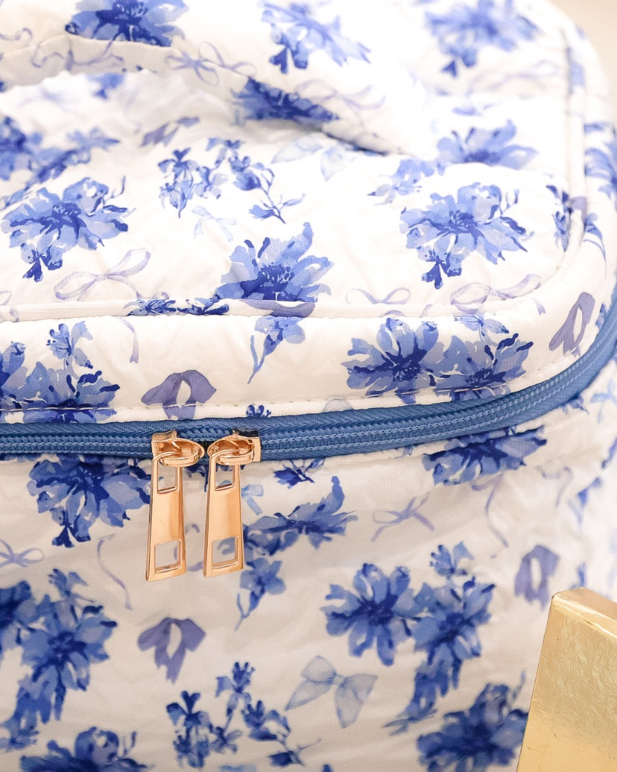 a structured bag with a spacious interior, a secure double zip around closure, a top handle, and gold accents on a quilted body in blue blossom (white/blue)