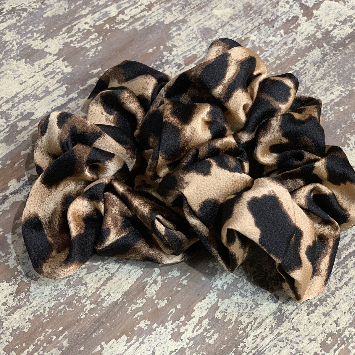 an oversized satin-look leopard scrunchie with glossy animal print fabric, plush gathered construction, lightweight feel, and gentle hair-friendly hold in leopard beige