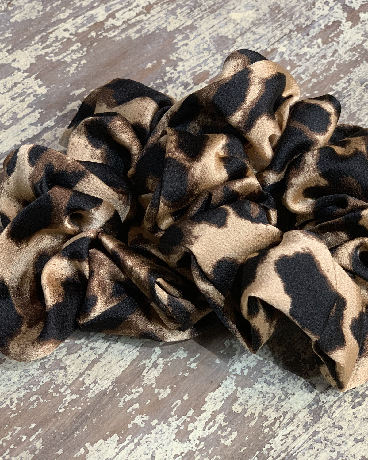 an oversized satin-look leopard scrunchie with glossy animal print fabric, plush gathered construction, lightweight feel, and gentle hair-friendly hold in leopard beige