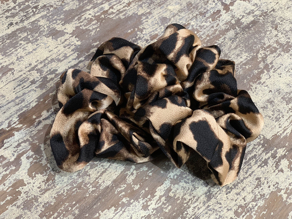 an oversized satin-look leopard scrunchie with glossy animal print fabric, plush gathered construction, lightweight feel, and gentle hair-friendly hold in leopard beige
