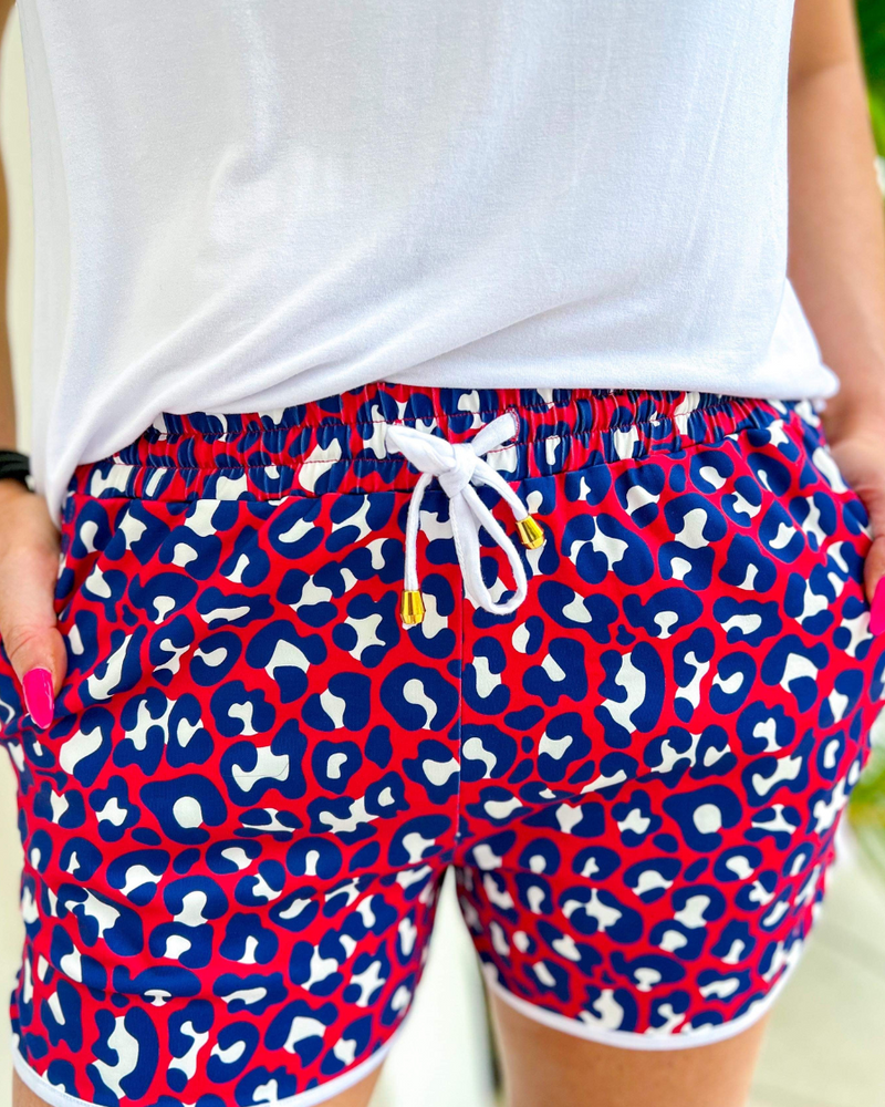 mid-rise relaxed fit activewear shorts with side pockets and a tie waist drawstring with gold bead accents, designed on a vibrant red leopard print and ivory trim