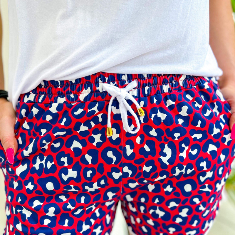 mid-rise relaxed fit activewear shorts with side pockets and a tie waist drawstring with gold bead accents, designed on a vibrant red leopard print and ivory trim