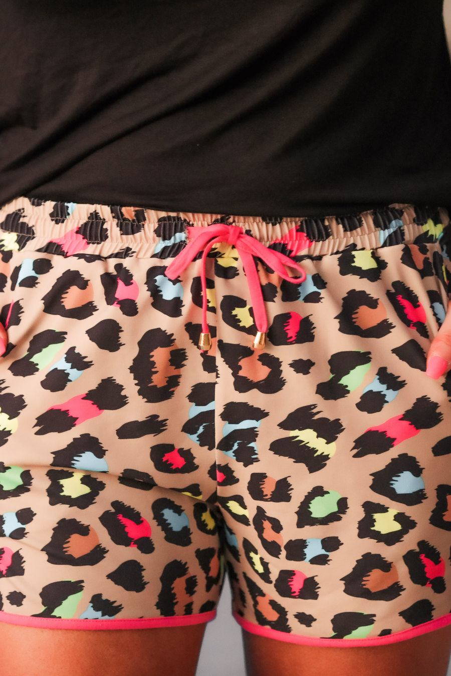 mid-rise relaxed fit activewear shorts with side pockets and a tie waist drawstring with gold bead accents, designed on a vibrant multicolor leopard pattern print fabric, tan base, and pink trim