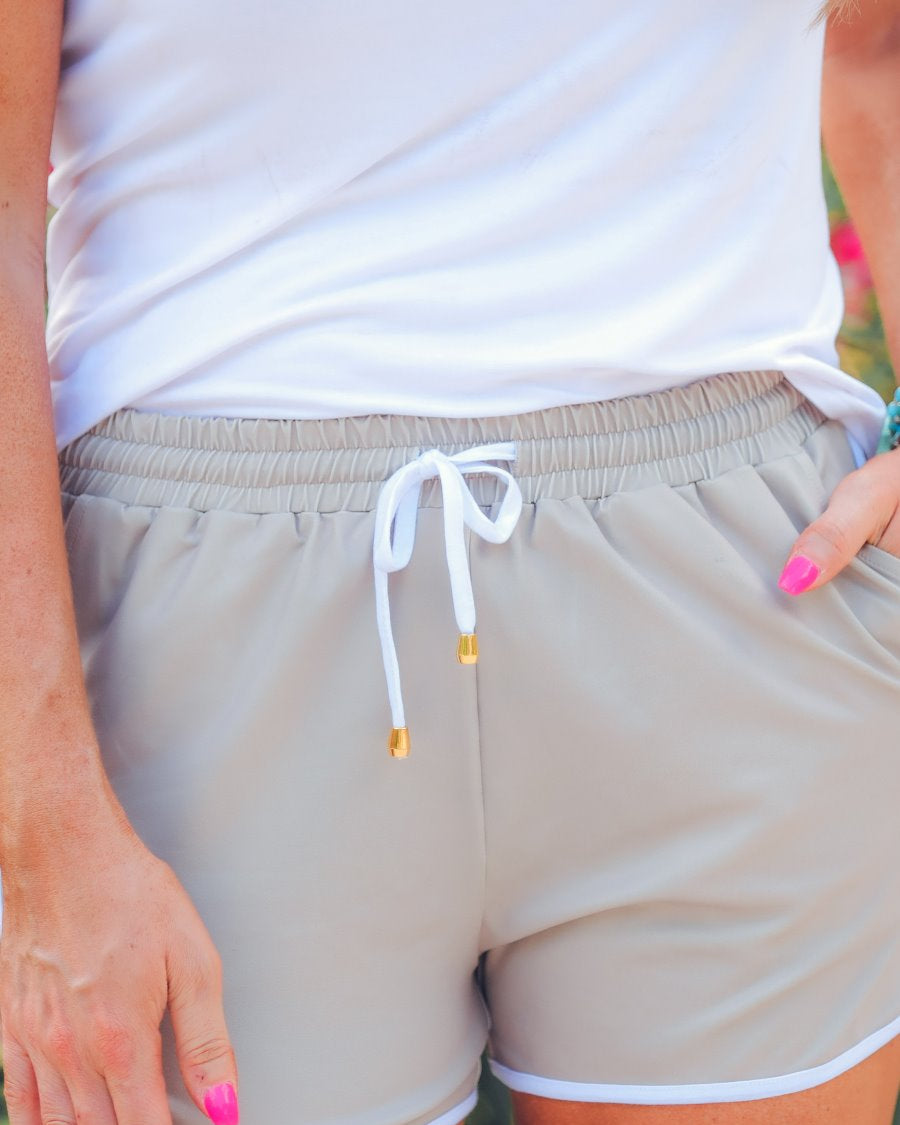 mid-rise relaxed fit activewear shorts with side pockets and a tie waist drawstring with gold bead accents, designed on a solid natural print fabric and ivory trim