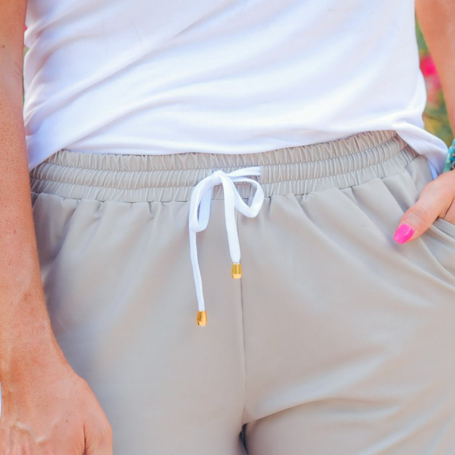 mid-rise relaxed fit activewear shorts with side pockets and a tie waist drawstring with gold bead accents, designed on a solid natural print fabric and ivory trim