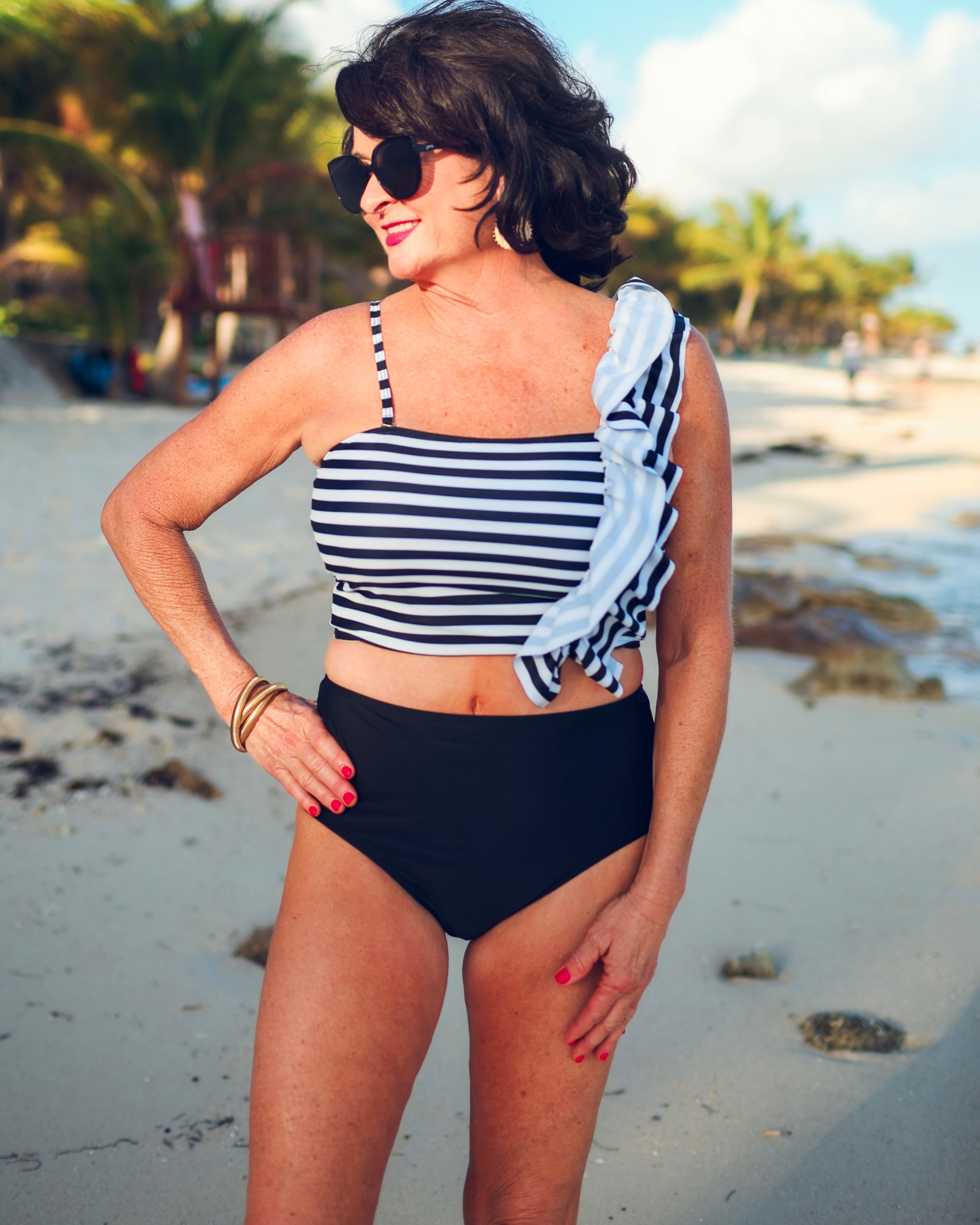 a two-piece swimsuit sold separately made of stretchy material with a black and white striped crop top, one chunky ruffle strap, one adjustable removable spaghetti strap, and coordinating solid black high-waisted bottoms