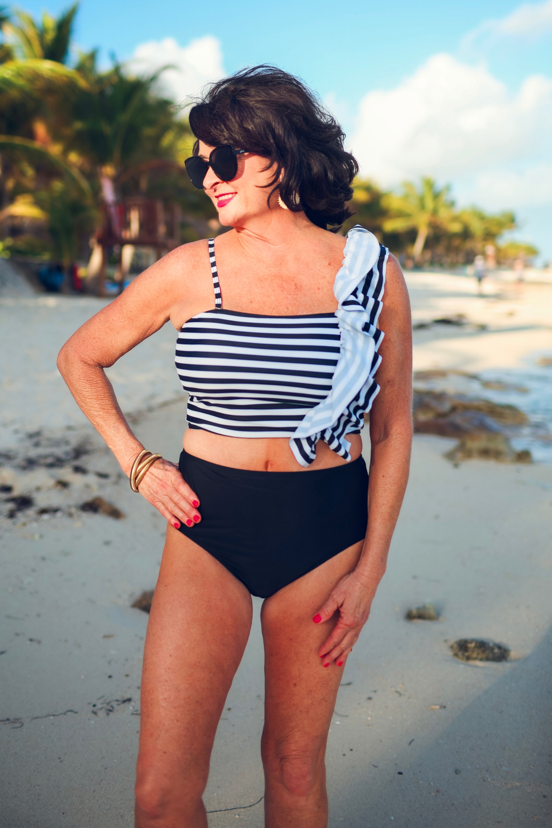 a two-piece swimsuit sold separately made of stretchy material with a black and white striped crop top, one chunky ruffle strap, one adjustable removable spaghetti strap, and coordinating solid black high-waisted bottoms