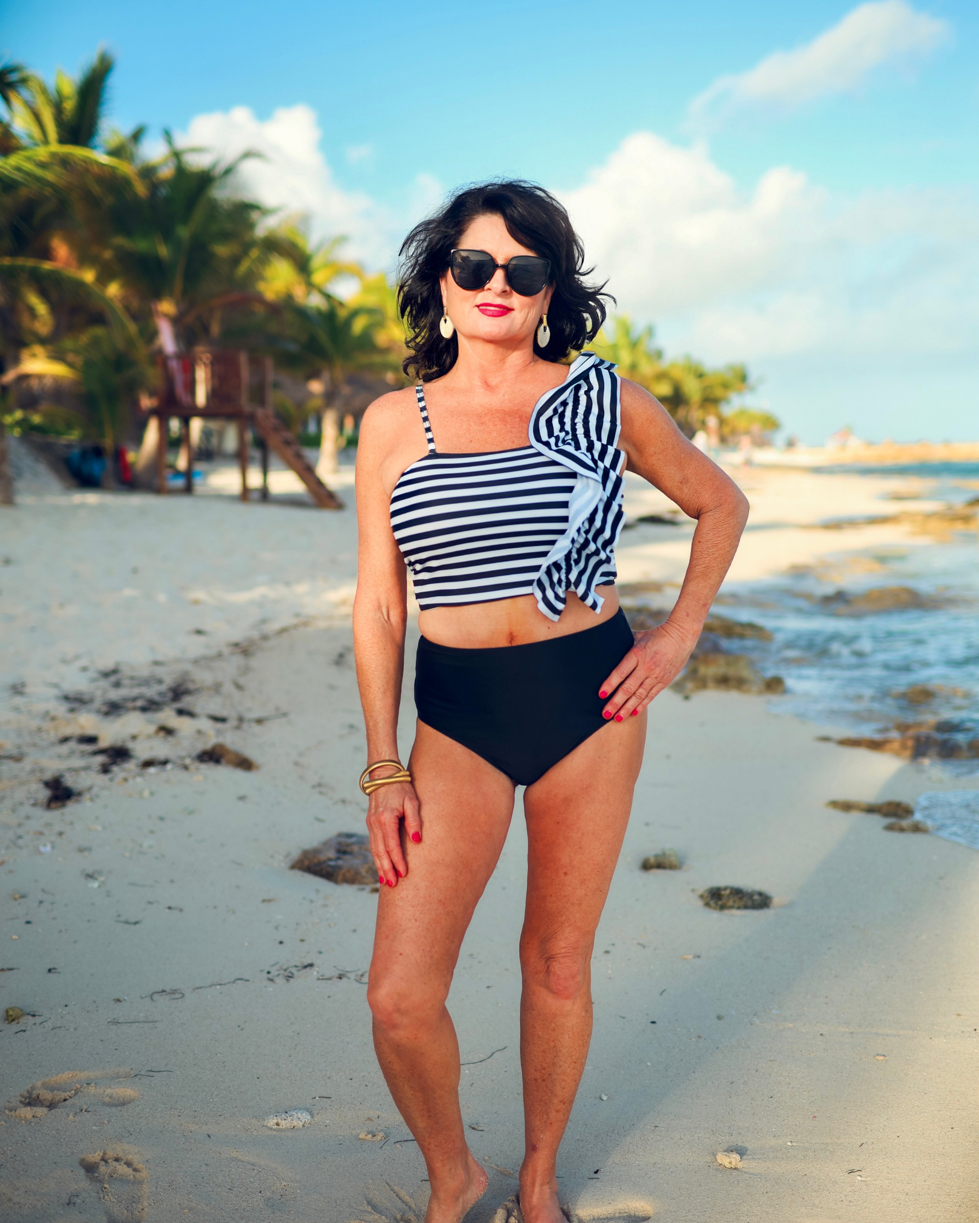 a two-piece swimsuit sold separately made of stretchy material with a black and white striped crop top, one chunky ruffle strap, one adjustable removable spaghetti strap, and coordinating solid black high-waisted bottoms